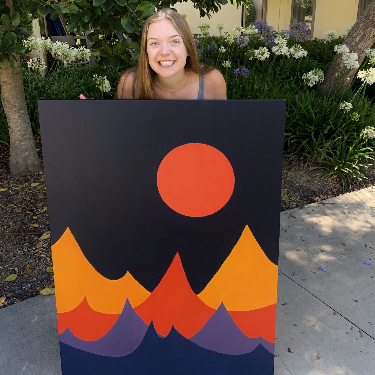 Elke holding up a large colorful painting of mountains.